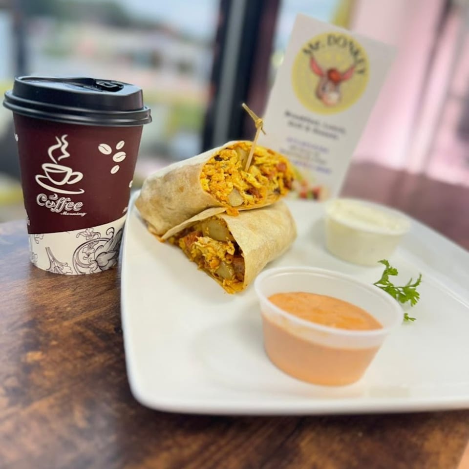 Two Mr Donkey burritos, a coffee cup, and two dipping sauces on a white plate.