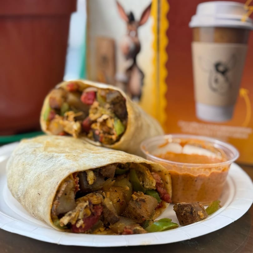 Two Mr Donkey burritos, cut in half, with a side of sauce and a coffee cup in the background.