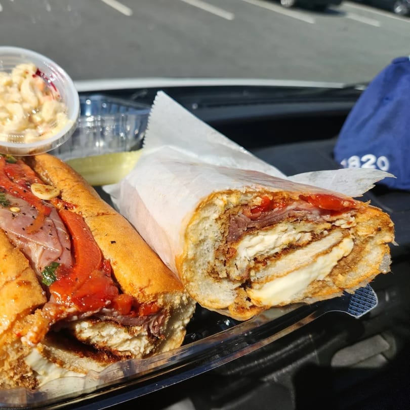 Two large sandwiches with various fillings, a pickle, and a side of macaroni salad.