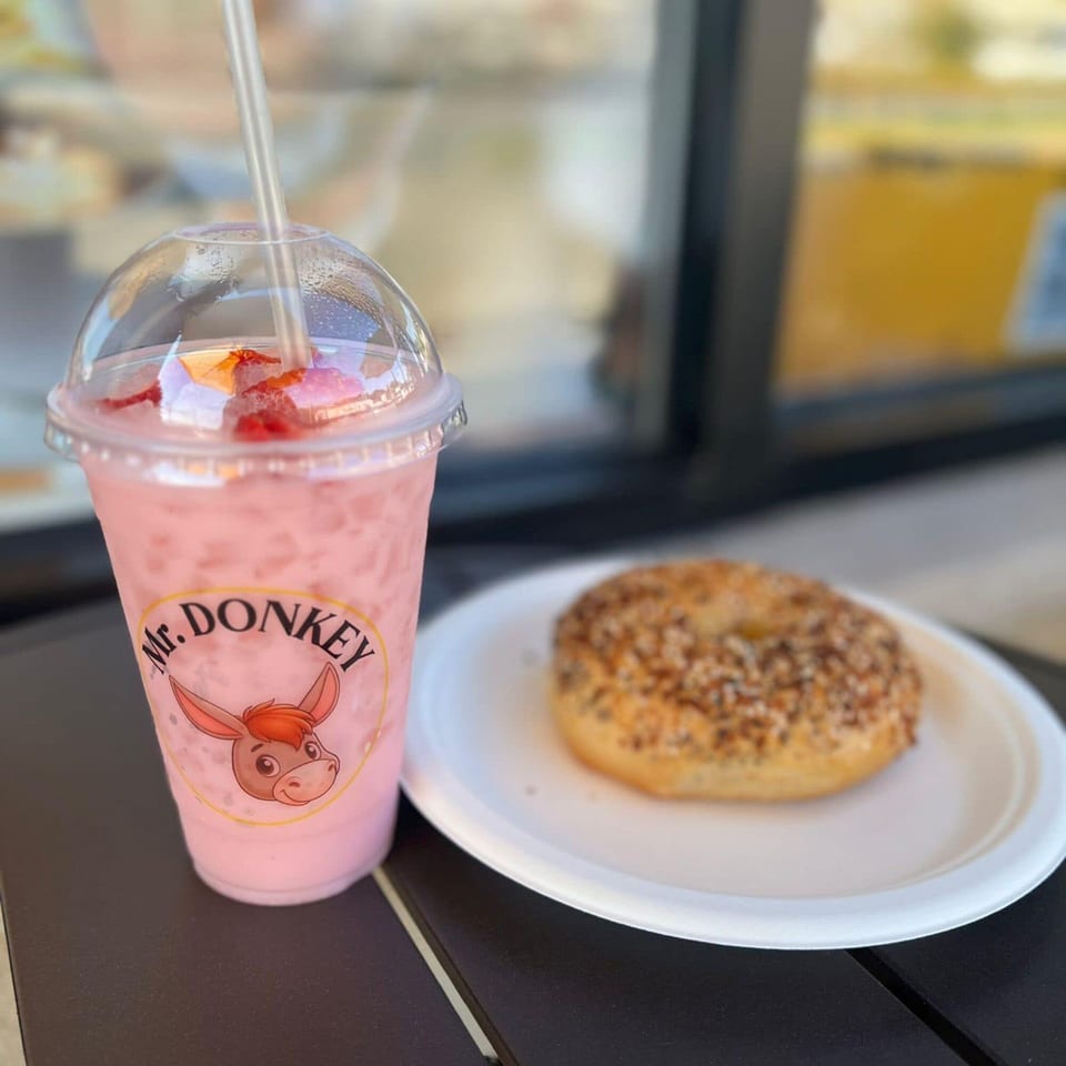A pink Mr. Donkey branded drink with a straw and a bagel on a white plate.