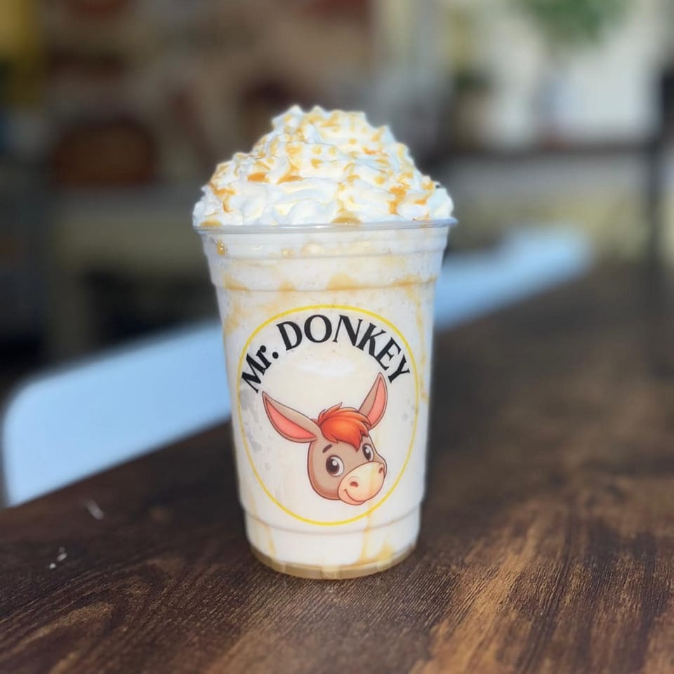 Mr. Donkey's caramel milkshake with whipped cream and caramel drizzle on a wooden table.