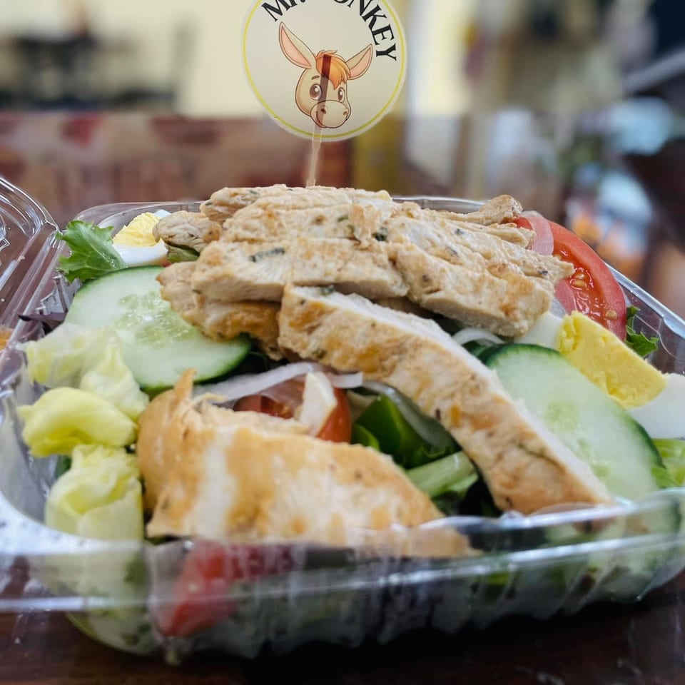 Mr Donkey's chicken salad with lettuce, cucumber, tomato, and egg in a clear plastic container.