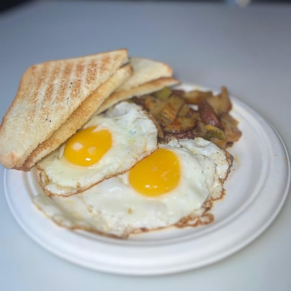Two fried eggs with golden yolks, toasted bread, and seasoned potatoes on a white plate.