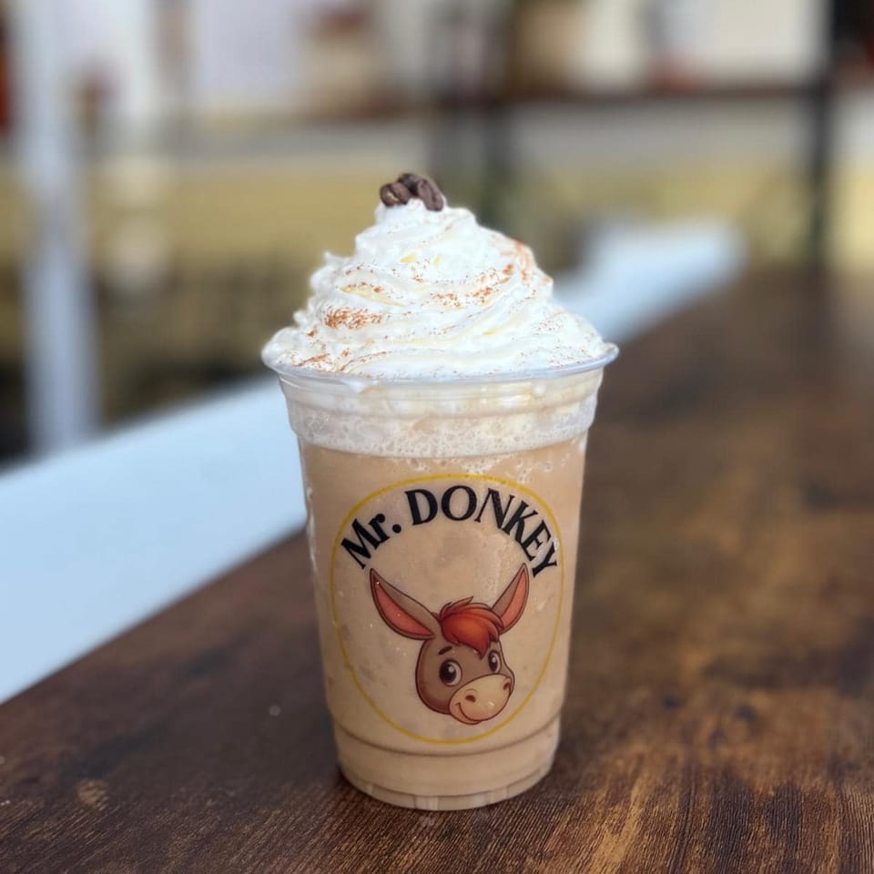 Mr. Donkey branded drink with whipped cream, cinnamon, and coffee beans on a wooden surface.