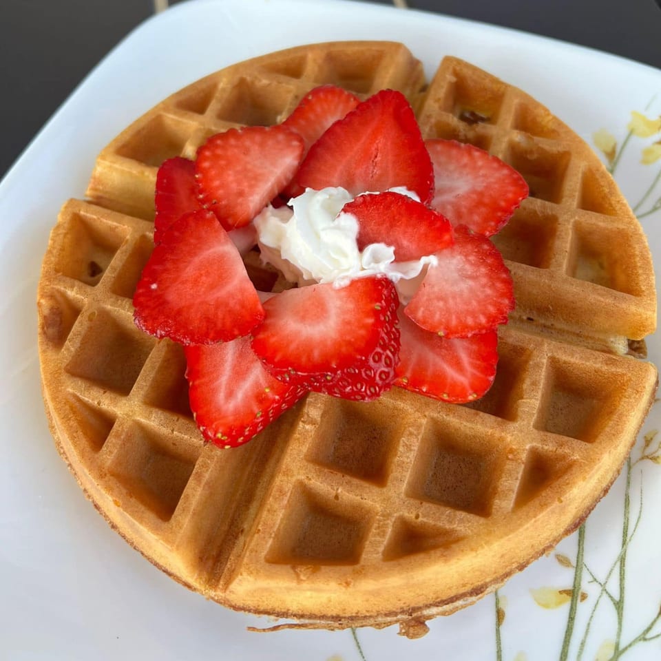 Golden waffle topped with sliced strawberries and a dollop of whipped cream on a white plate.